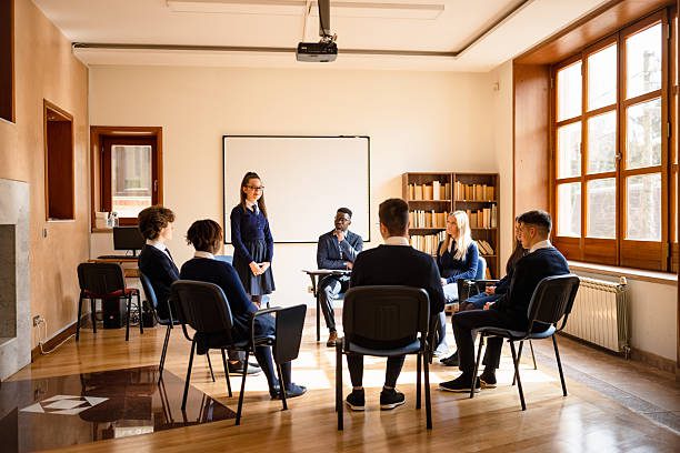 A professional group meeting taking place in a well-lit classroom. Participants are seated in a circle, engaging in discussion and collaboration.